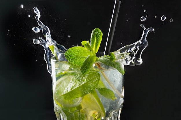 Spritzer Mojito-Cocktail oder Limonade mit Limette und Minze im Glas auf Schwarz Nahaufnahme Sommergetränk