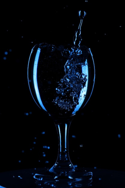 Spritzer und Wassertropfen in einem Glas sind auf schwarzem Hintergrund isoliert. Blaues Wasser im Glas