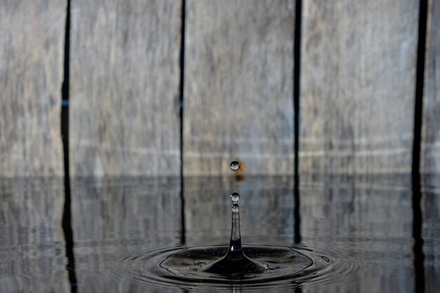 Spritzer und Wellen auf dem Wasser von gefallenen Regentropfen auf Holzhintergrund.