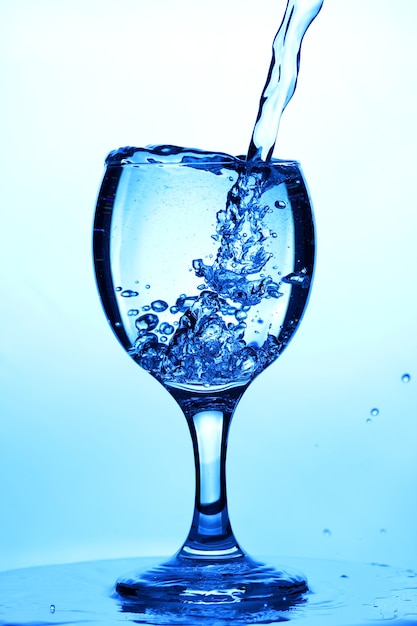 Spritzwasser in ein Glas. Gießen von Wasser in Glas auf blauem Hintergrund