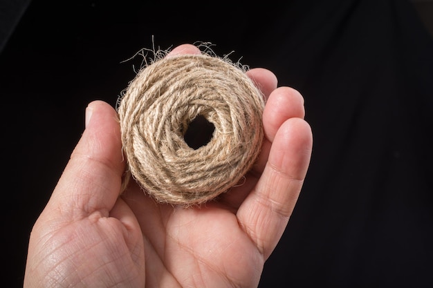 Spule aus brauner Schnur in der Hand auf schwarzem Hintergrund