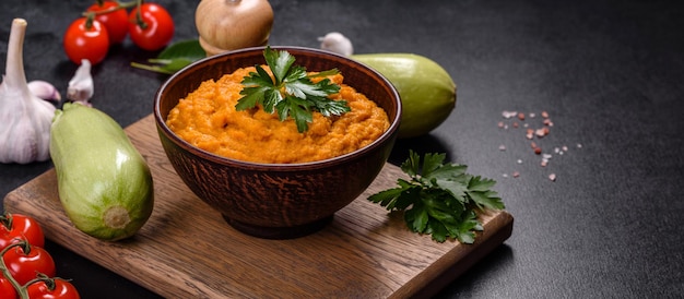 Squash-Kaviar mit Knoblauch und Tomaten in einer rustikalen Schüssel auf dunklem Hintergrund