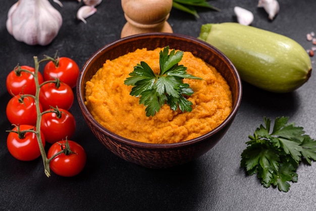 Squash-Kaviar mit Knoblauch und Tomaten in einer rustikalen Schüssel auf dunklem Hintergrund