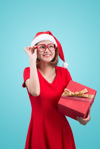 Sra. Santa. Bela jovem asiática com chapéu de Papai Noel segurando um presente isolado em azul.