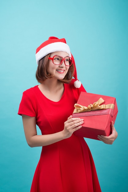 Sra. Santa. Bela jovem asiática com chapéu de Papai Noel segurando um presente isolado em azul.