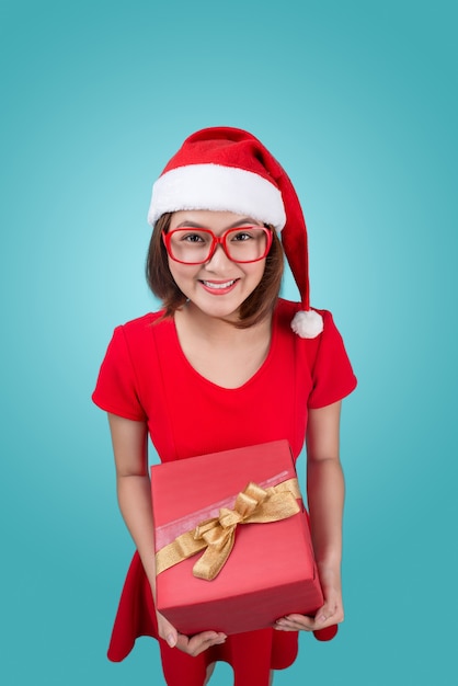 Sra. Santa. Hermosa joven asiática con sombrero de santa sosteniendo un regalo aislado en azul.