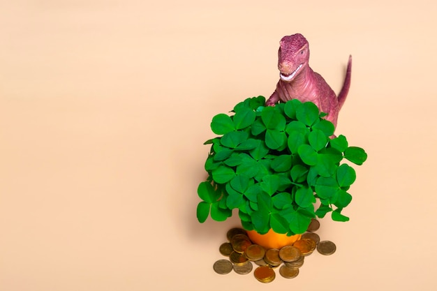St. Patricks Day Happy Dinosaurier ein Strauß Klee in einem Eimer und Goldmünzen auf beigem Hintergrund Nahaufnahme mit Kopierraum