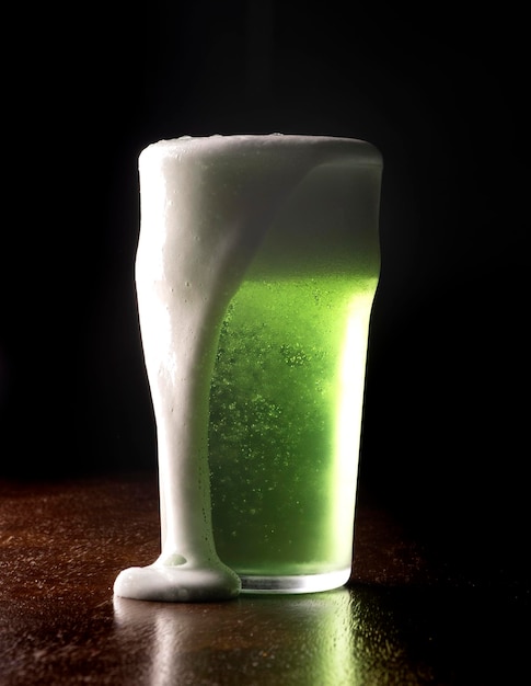 St Patricks pinta de cerveza verde vertiendo espuma en la mesa de madera