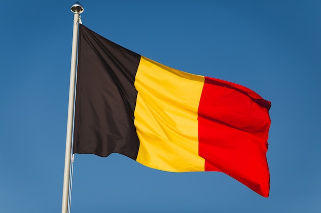 Foto staatsflagge von belgien auf fahnenmast vor blauem himmel. schwarze, gelbe und rote farben