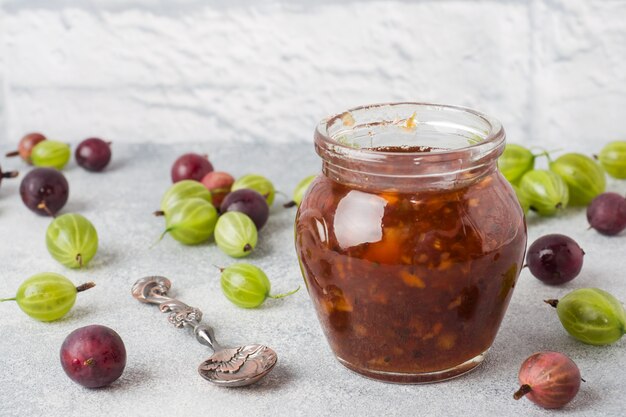 Stachelbeermarmelade in einem Glas mit frischen Stachelbeerbeeren auf einer grauen Oberfläche