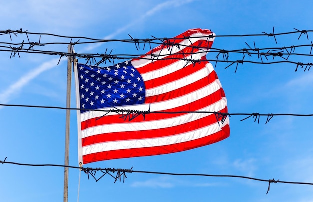 Stacheldrahtzaun vor der Flagge der Vereinigten Staaten von Amerika weht im Wind