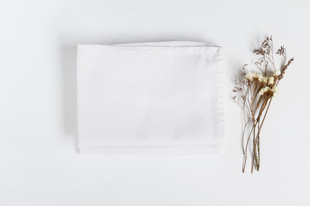 Foto stack de tecidos com flores secas sobre fundo claro flat lay com pano de linho dobrado branco para mock up