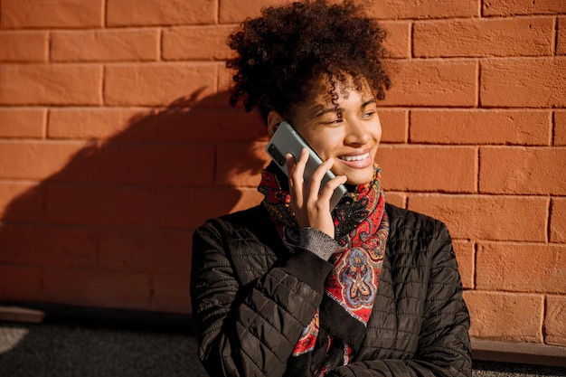 Stadt leben. Dunkelhaariges junges Mädchen mit einem Telefon auf einem Backsteinmauerhintergrund