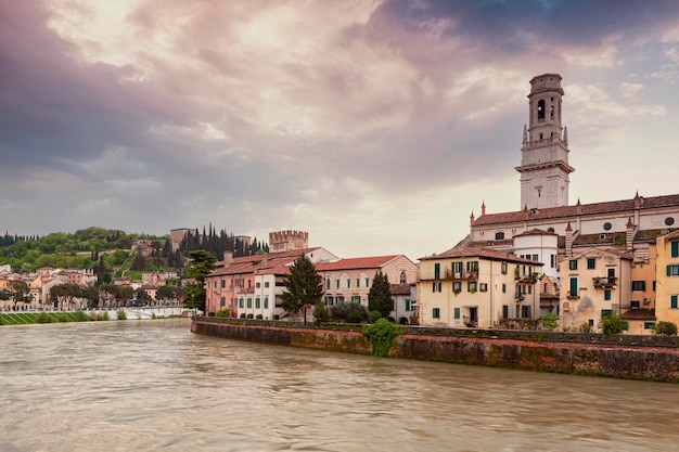 Stadt Verona im Morgengrauen. Ein Fluss mit einer Kirche auf der linken Seite und dem Wort Verona auf der rechten Seite.