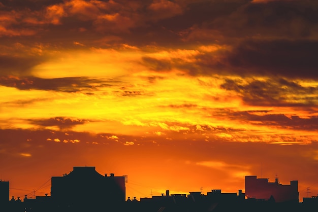 Stadtbild mit lebhafter feuriger Morgendämmerung. Erstaunlich warmer dramatischer bewölkter Himmel über dunklen Silhouetten von Stadtgebäuden. Orange Sonnenlicht. Atmosphärischer Hintergrund des Sonnenaufgangs bei bewölktem Wetter. Speicherplatz kopieren.