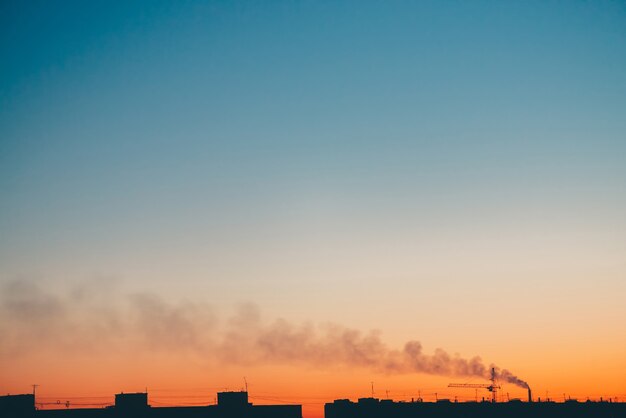 Stadtbild mit wunderbarer bunter lebendiger Morgendämmerung. Erstaunlicher blauer Himmel mit orangefarbenem sonnigem Licht über dunklen Silhouetten von Stadtgebäuden.