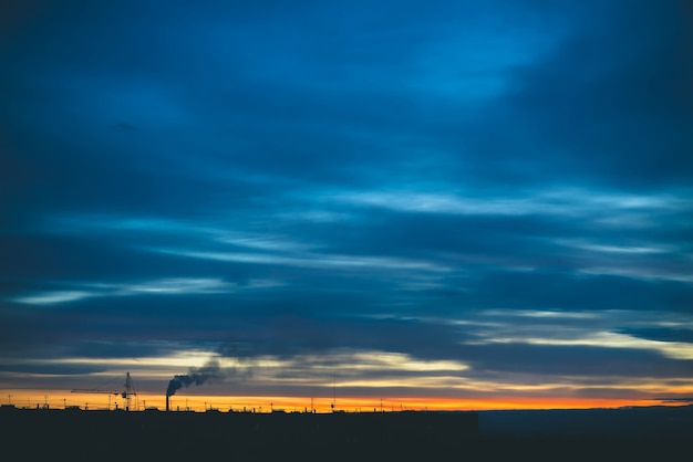 Stadtbild mit wunderschöner bunter, lebendiger Morgendämmerung. Erstaunlicher dramatischer blauer bewölkter Himmel über dunklen Silhouetten von Stadtgebäuden. Atmosphärischer Hintergrund des orangefarbenen Sonnenaufgangs bei bewölktem Wetter. Speicherplatz kopieren.