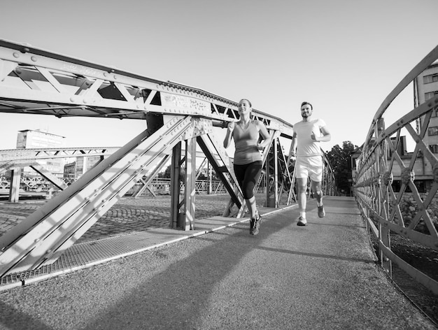 Stadtsport, gesundes junges Paar, das am sonnigen Morgen über die Brücke in der Stadt joggt