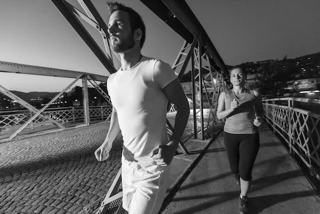 Stadtsport, gesundes Paar, das am frühen Morgen in der Nacht über die Brücke in der Stadt joggt