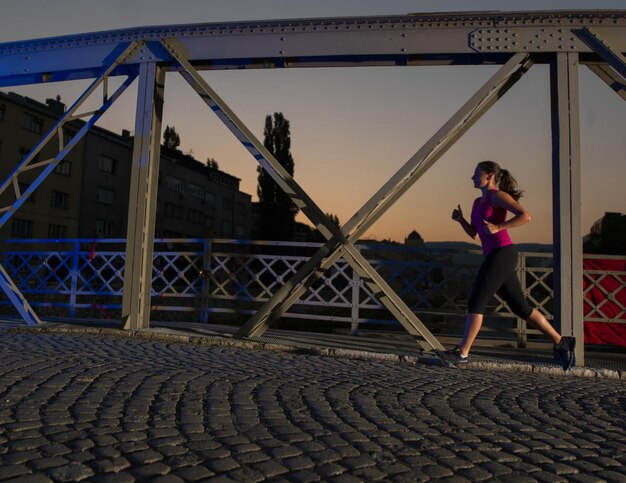 Stadtsport, junge gesunde Frau, die am frühen Morgen in der Nacht über die Brücke in der Stadt joggt