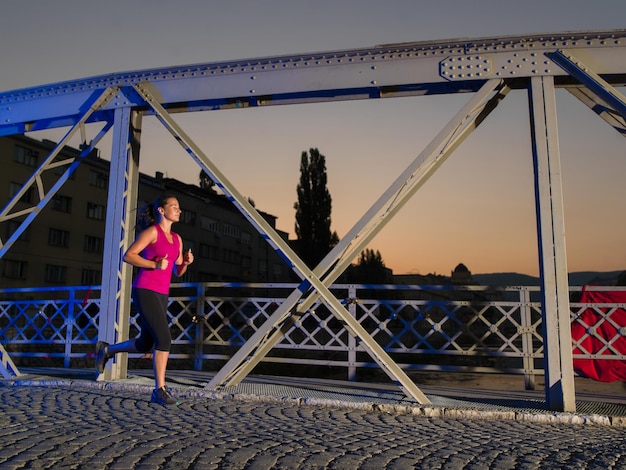 Stadtsport, junge gesunde Frau, die am frühen Morgen in der Nacht über die Brücke in der Stadt joggt