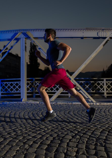 stadtsport, junger gesunder mann, der am frühen morgen in der nacht über die brücke in der stadt joggt