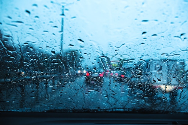 Stadtstraße durch Windschutzscheibenautos abstrakter Hintergrundwassertropfen auf den Glaslichtern und -regen.