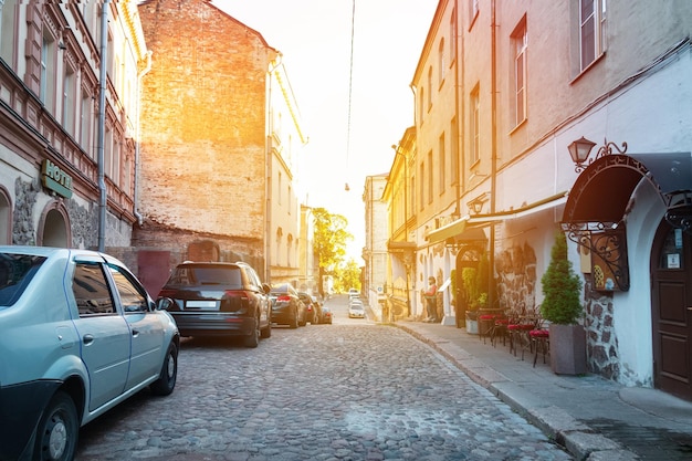 Stadtstraße mit Pflastersteinhäusern und geparkten Autos Sonnenuntergang zwischen Gebäuden