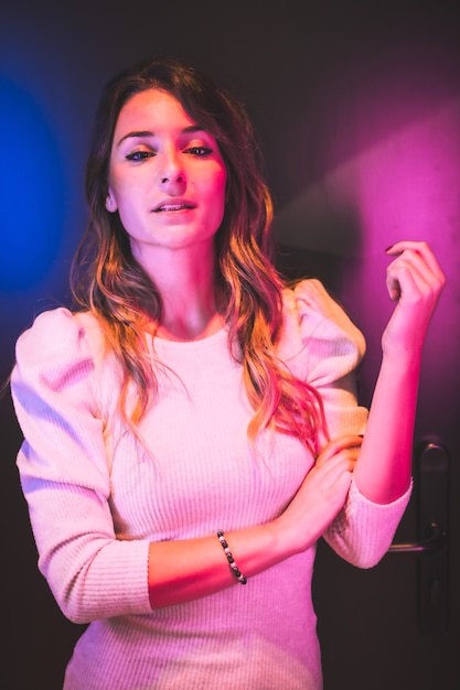 Städtisches Porträt einer schönen jungen Frau, die mit rosa und blauen LED-Lichtern auf schwarzem Hintergrund in die Kamera schaut