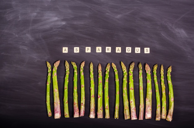 Stängel frischer grüner Spargel auf einer schwarzen Kreidetafel. Saisonale Frühjahrsernte. Flach legen, Platz kopieren. Gesundes Lebensmittelkonzept. Von oben betrachten.