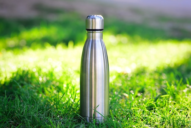 Stahl-thermowasserflasche aus silber auf dem hintergrund von verschwommenem gras mit kopierraum