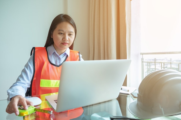 Stahlfrau des Porträts Asien-Fraueningenieur, die Standort mit ihrem Laptop an der Baustelle überprüft