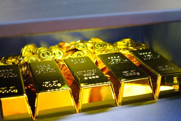 Stahltresorbox voller Goldbarrenstapel und Münzen