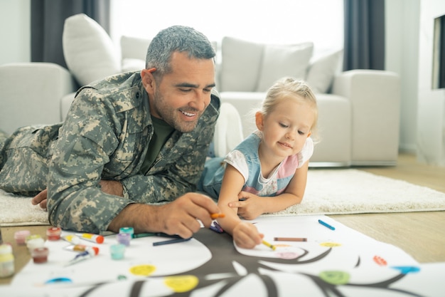 Stammbaum malen. Hübscher glücklicher Militärdiener und seine Tochter malen gemeinsam den Stammbaum