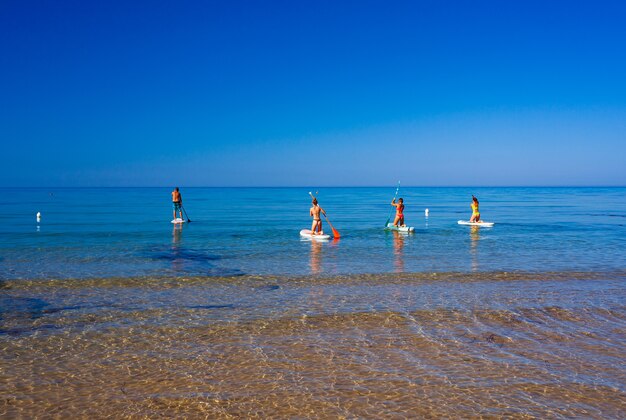 Stand up paddle boarding. Alegre grupo de amigos entrenando tabla de SUP en el mar Mediterráneo en una mañana soleada en la playa de Realmonte, Sicilia. Italia