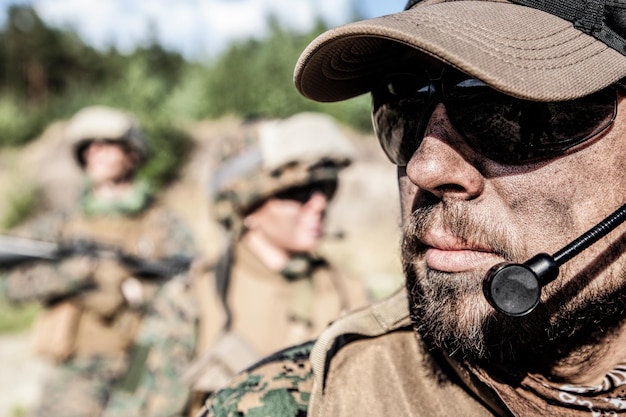 Standortaufnahme von United States Marine mit Gewehrwaffen in Uniformen. Militärische Ausrüstung, Armeehelm, Kriegsbemalung, geräuchertes schmutziges Gesicht, taktische Handschuhe. Waffen, Armee, Patriotismus-Konzept