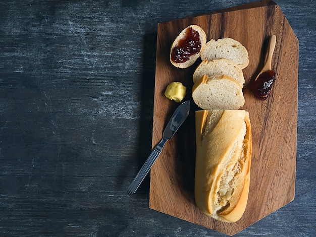 Stangenbrot auf hölzernem Brett mit Erdbeermarmelade und Butter