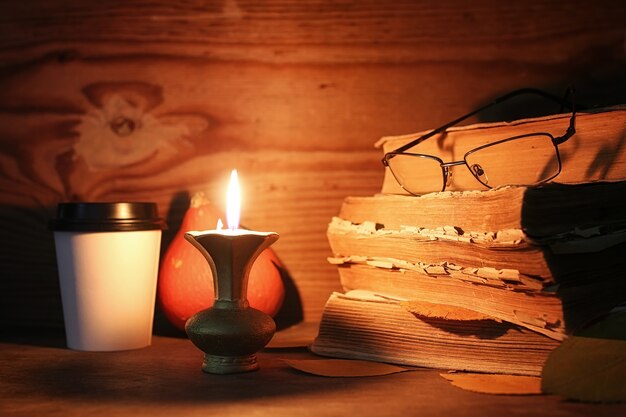 Stapel altes zerfetztes Buch auf einem Holztisch beleuchtete Kerze und Gläser