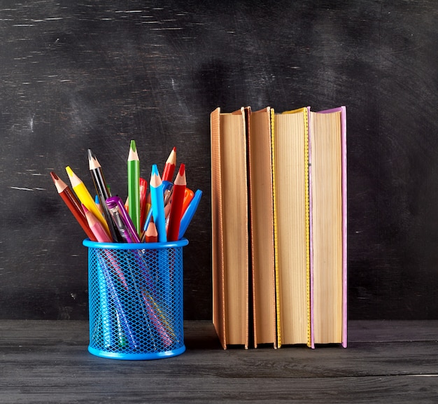 Stapel Bücher und blaues Briefpapierglas mit mehrfarbigen hölzernen Bleistiften