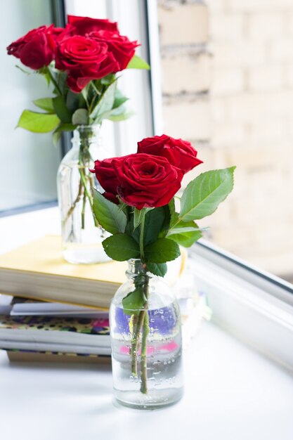 Stapel Bücher und Rosen in Vasen in der Nähe eines offenen Fensters