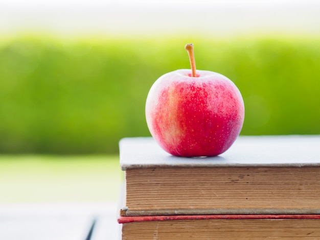 Stapel Bücher und roter Apfel auf Holztisch.