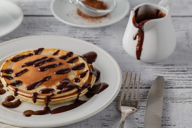 Stapel der köstlichen Pfannkuchen mit Schokolade auf Teller und Serviette auf hölzernem Hintergrund