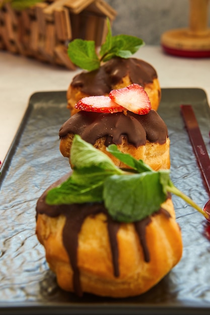 Stapel Eclair von Profiteroles mit dunkler geschmolzener Schokolade auf einem schwarzen Teller.