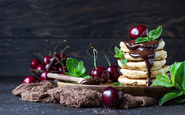 Stapel flaumige Pfannkuchen oder Stückchen mit Schokoladen- und Kirschmarmelade, frischer Kirsche und Minze.