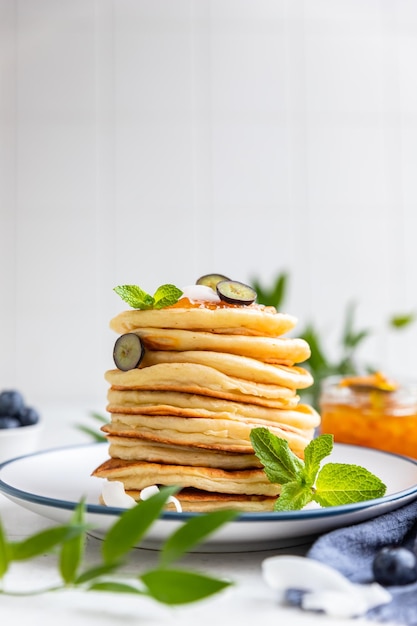 Stapel flauschiger Pfannkuchen mit Orangenmarmelade, Heidelbeeren, Kokoschips und Minze Traditionelles Frühstück