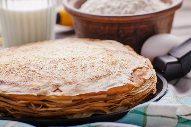 Stapel französische Crpes in Bratpfanne auf Holzküchentisch mit Milcheiern und Mehl beiseite