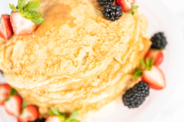 Stapel frisch gebackener Crêpes mit Beeren auf einem Tortenständer.