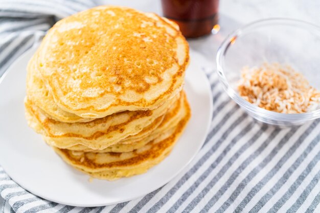 Stapel frisch gebackener Kokos-Bananen-Pfannkuchen, garniert mit geschnittenen Bananen, gerösteter Kokosnuss und Ahornsirup.