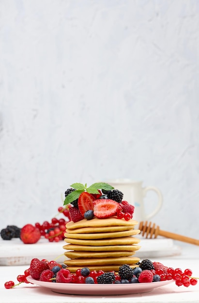 Stapel gebackener Pfannkuchen mit Früchten in einem runden Teller auf einem weißen Tisch leckeres Frühstück