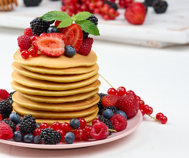 Stapel gebackener Pfannkuchen mit Früchten in einem runden Teller auf einem weißen Tisch